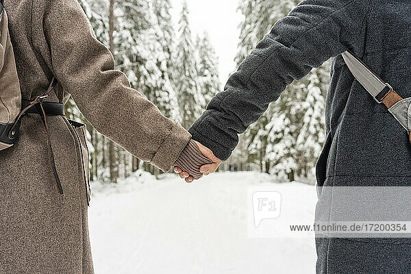 Paar in warmer Kleidung hält sich an den Händen  während es im Wald steht