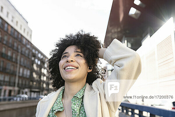Smiling Afro woman with hand in hair at street during sunny day