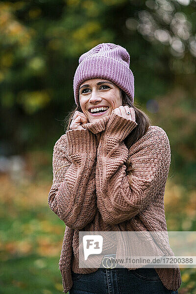 Porträt einer schönen Frau mit rosa Strickmütze und Pullover  die im Freien steht und lächelt