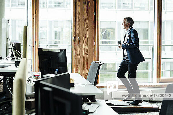 Lächelnder Geschäftsmann schaut weg  während er auf dem Laufband im Büro trainiert