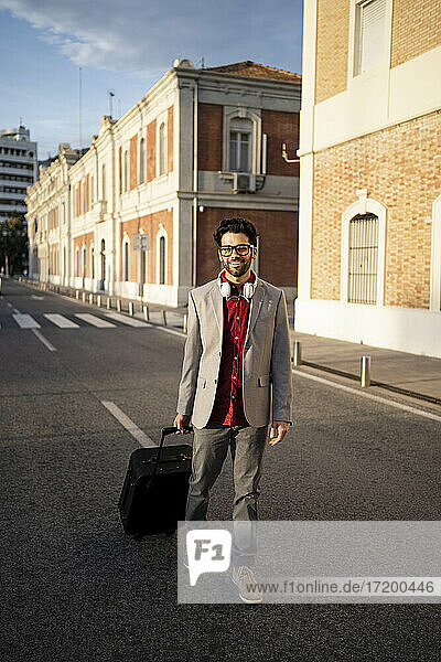 Smiling male entrepreneur with suitcase walking on road