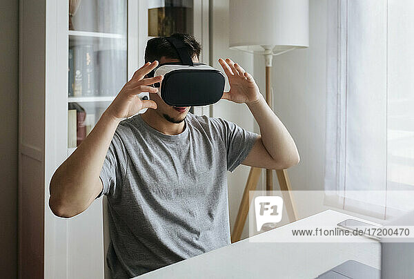 Männlicher Unternehmer mit Virtual-Reality-Headset  während er im Büro zu Hause sitzt