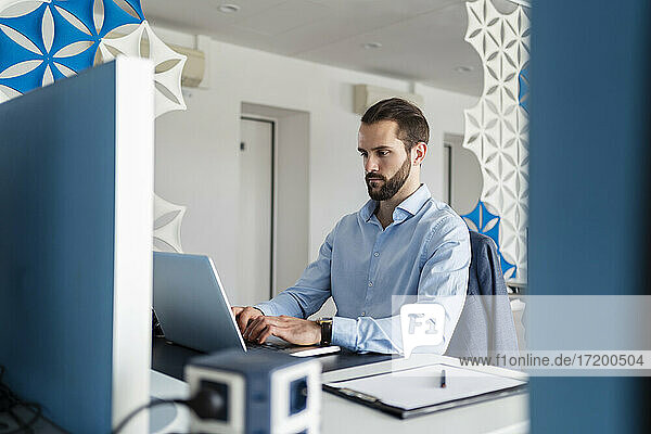 Männlicher Unternehmer  der einen Laptop benutzt  während er am Schreibtisch im Büro sitzt