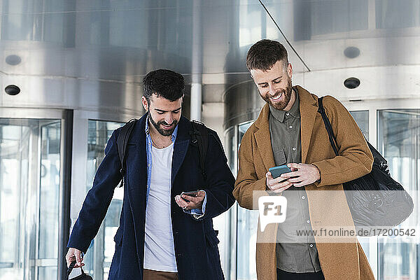 Business partners using mobile phones while standing with bag against building