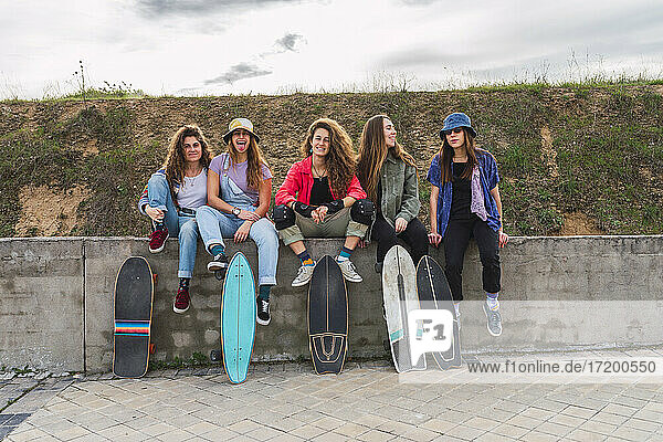 Fröhliche Freundinnen mit Skateboards auf einer Stützmauer sitzend