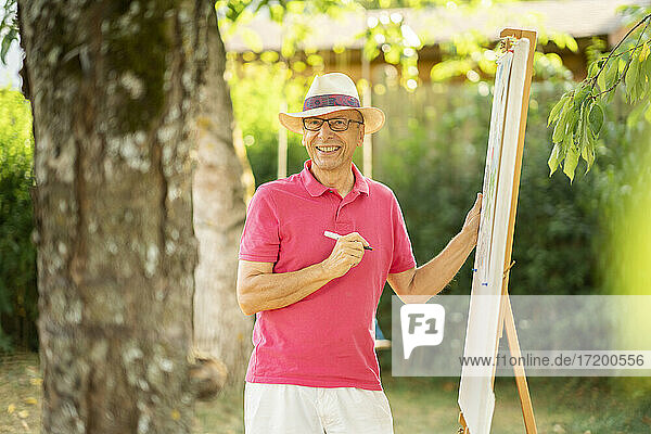 Happy senior man standing by easel at back yard garden