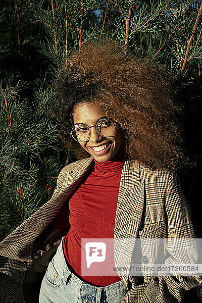 Lächelnde Afro-Frau mit Brille steht vor Pflanzen