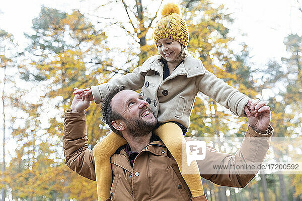 Lächelnder Vater  der seine Tochter auf den Schultern trägt  während er im Wald steht