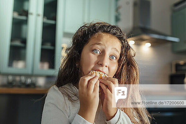 Mädchen mit braunem Haar isst Mandarine  während sie am Esstisch in der Küche sitzt