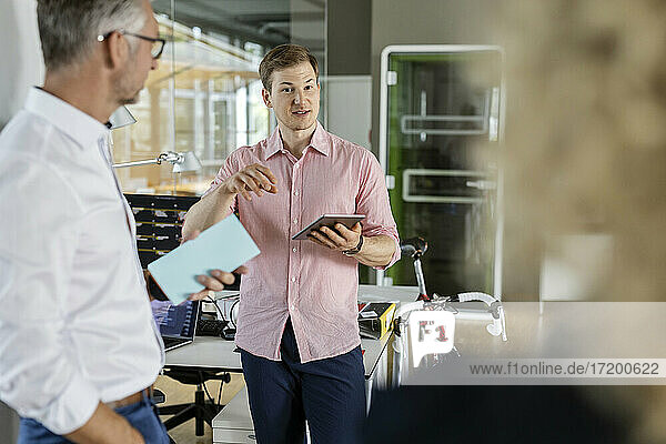 Young businessman with digital tablet explaining plans to colleagues in office