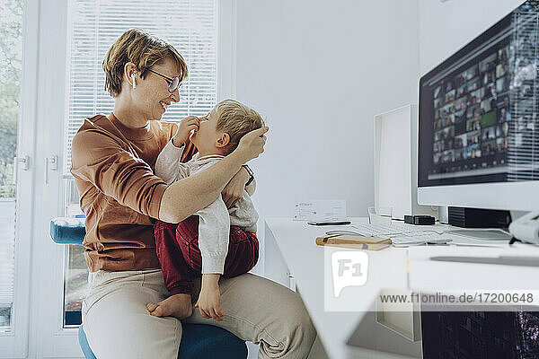 Liebevolle Mutter  die ihren Sohn umarmt  der auf ihrem Schoß im Büro sitzt
