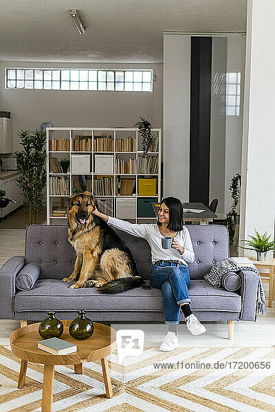 Young woman stroking pet dog while sitting on sofa in living room