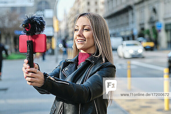 Lächelnde Frau  die auf der Straße einen Vlog über ihr Handy führt