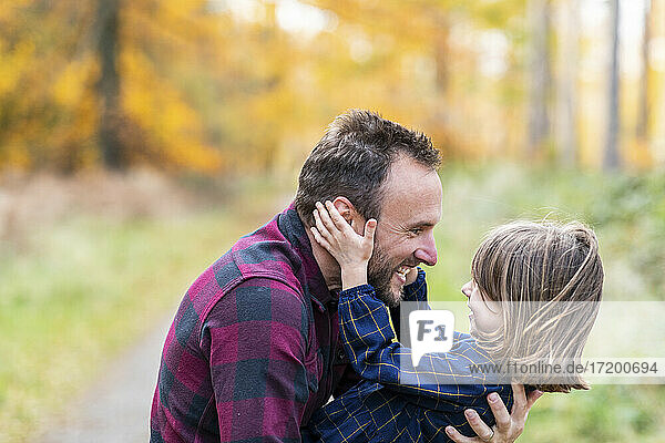 Lächelnder Vater trägt seine Tochter beim Spielen im Wald