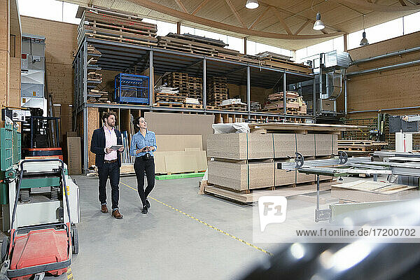 Male and female entrepreneurs discussing while walking in factory warehouse