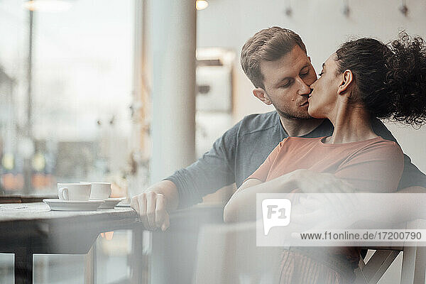 Junge Frau küsst Mann beim Zusammensitzen in einem Cafe