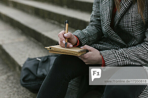 Frau schreibt in ein Buch  während sie auf einer Treppe sitzt