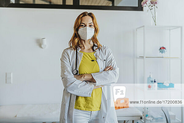 Selbstbewusste Ärztin mit Gesichtsschutzmaske  die mit verschränkten Armen in einer Klinik steht