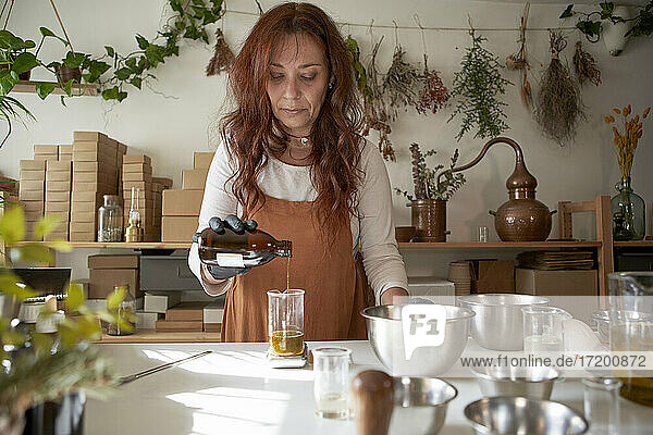 Mature woman pouring essential oil in beaker at workshop