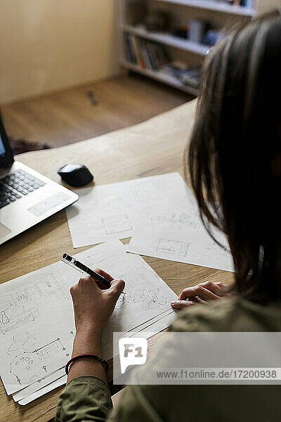 Weibliche Designerin  die am Schreibtisch in einer Werkstatt auf Papier zeichnet