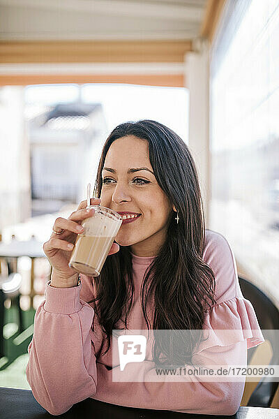 Smiling woman drinking coffee while sitting at coffee shop