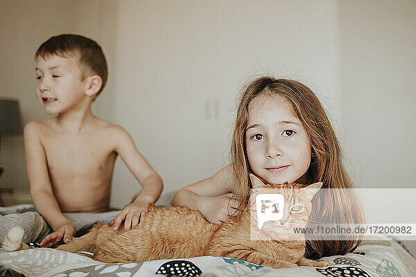Mädchen lehnt sich an eine Katze  während ihr Bruder im Schlafzimmer wegschaut