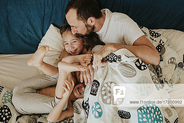 Vater küsst Tochter auf die Stirn  während Sohn lachend auf dem Bett zu Hause