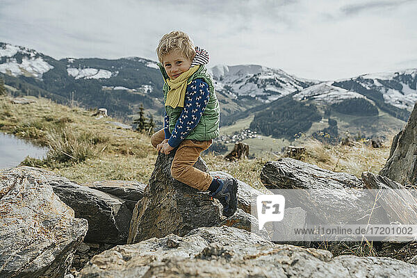 Smiling boy sitting on rock against sky at Salzburger Land  Leogang Mountains  Austria