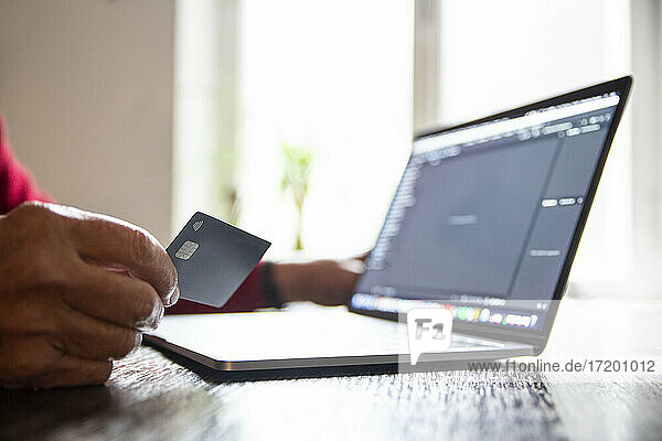 Senior man shopping online through laptop with credit card at home