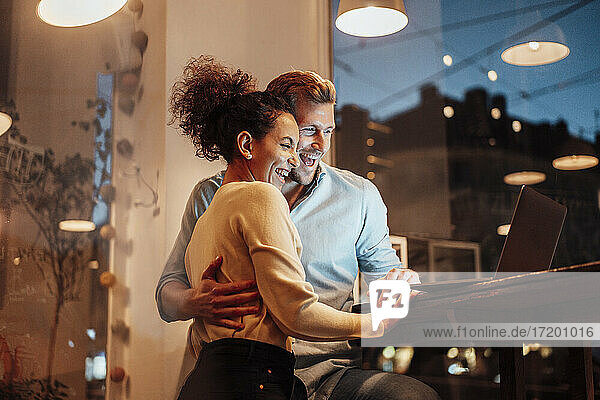 Glückliche Geschäftsleute  die gemeinsam in einem Café stehen und auf einen Laptop schauen