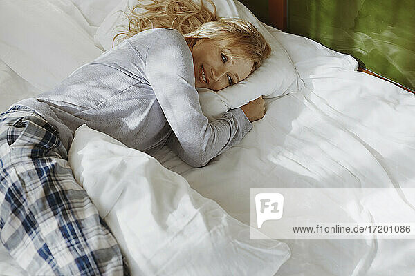 Blond woman in pajamas lying on bed at home