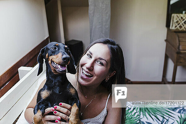 Laughing woman holding Dachshund dog on bed at home