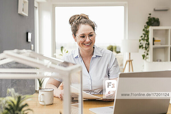 Lächelnde Unternehmerin mit Dokument am Schreibtisch sitzend