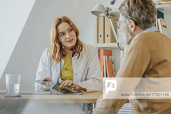 Allgemeinmediziner mit digitalem Tablet im Gespräch mit einem Patienten in der Arztpraxis