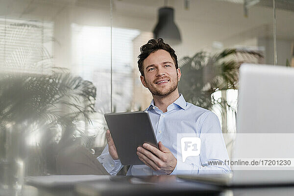Männlicher Unternehmer mit digitalem Tablet  der im Büro wegschaut