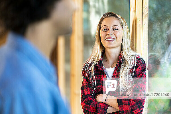 Lächelnde Frau  die einen Mann ansieht  während sie sich an ein Fenster lehnt