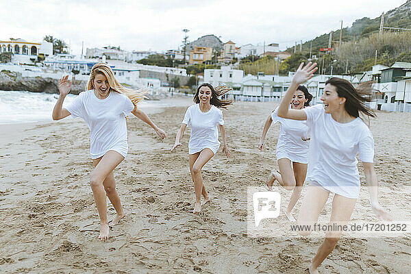 Young female friends running on sand while having fun during vacations