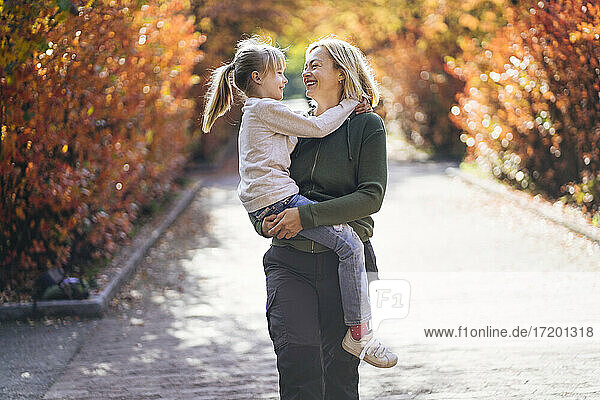 Smiling mother carrying daughter while walking in park