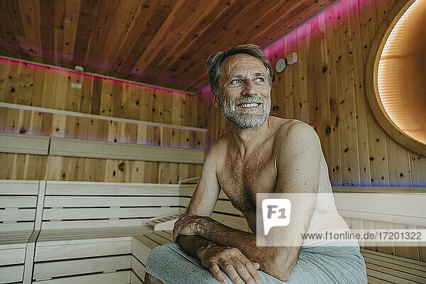 Smiling mature man looking away while sitting at finnish sauna