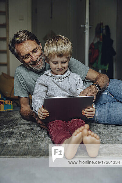 Smiling father watching son using tablet in bedroom