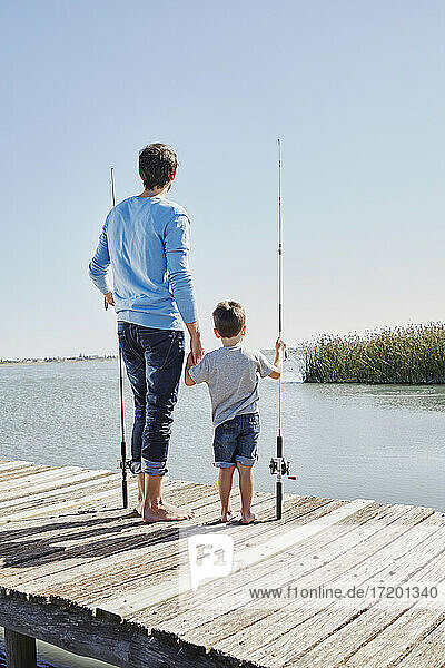 Vater und Sohn mit Angelruten  die sich an den Händen halten  während sie am Pier stehen