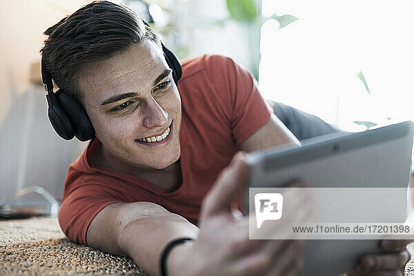 Lächelnder junger Mann mit drahtlosen Kopfhörern  der ein Video auf einem digitalen Tablet anschaut