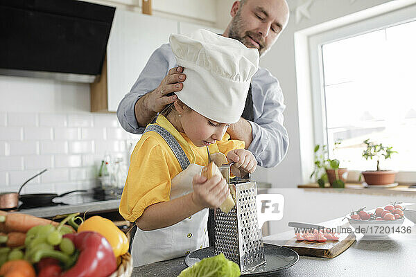 Reife Männer passen die Kochmütze eines Mädchens an  während sie in der Küche stehen