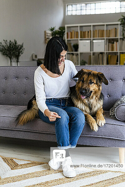 Frau mit deutschem Schäferhund sitzt zu Hause auf dem Sofa