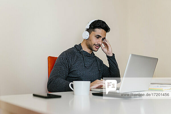Young man listening music while using laptop in living room
