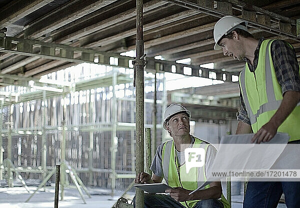 Männliche Bauarbeiter halten ein digitales Tablet  während sie mit einem Kollegen auf der Baustelle planen