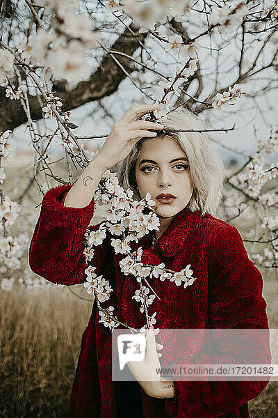 Beautiful blond woman standing holding twig of blossoming almond tree during spring