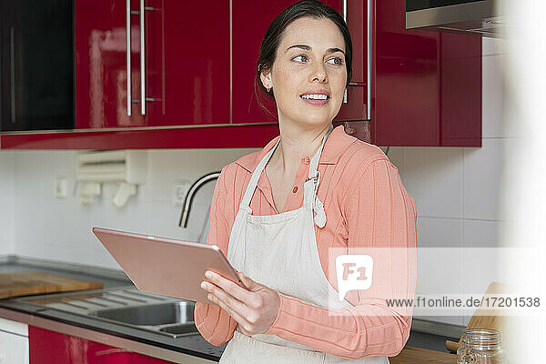 Schöne Frau schaut weg  während sie ein digitales Tablet in der Küche zu Hause hält