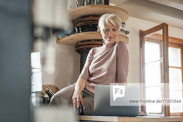 Female freelance worker with laptop sitting on kitchen counter at home
