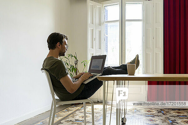 Junger männlicher Unternehmer arbeitet am Laptop  während er am Tisch im Büro sitzt
